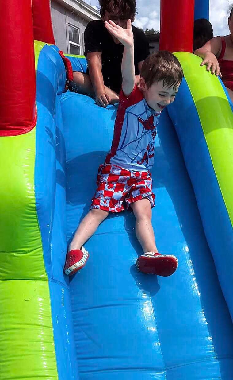 Boy waving while sliding down a colorful inflatable water slide