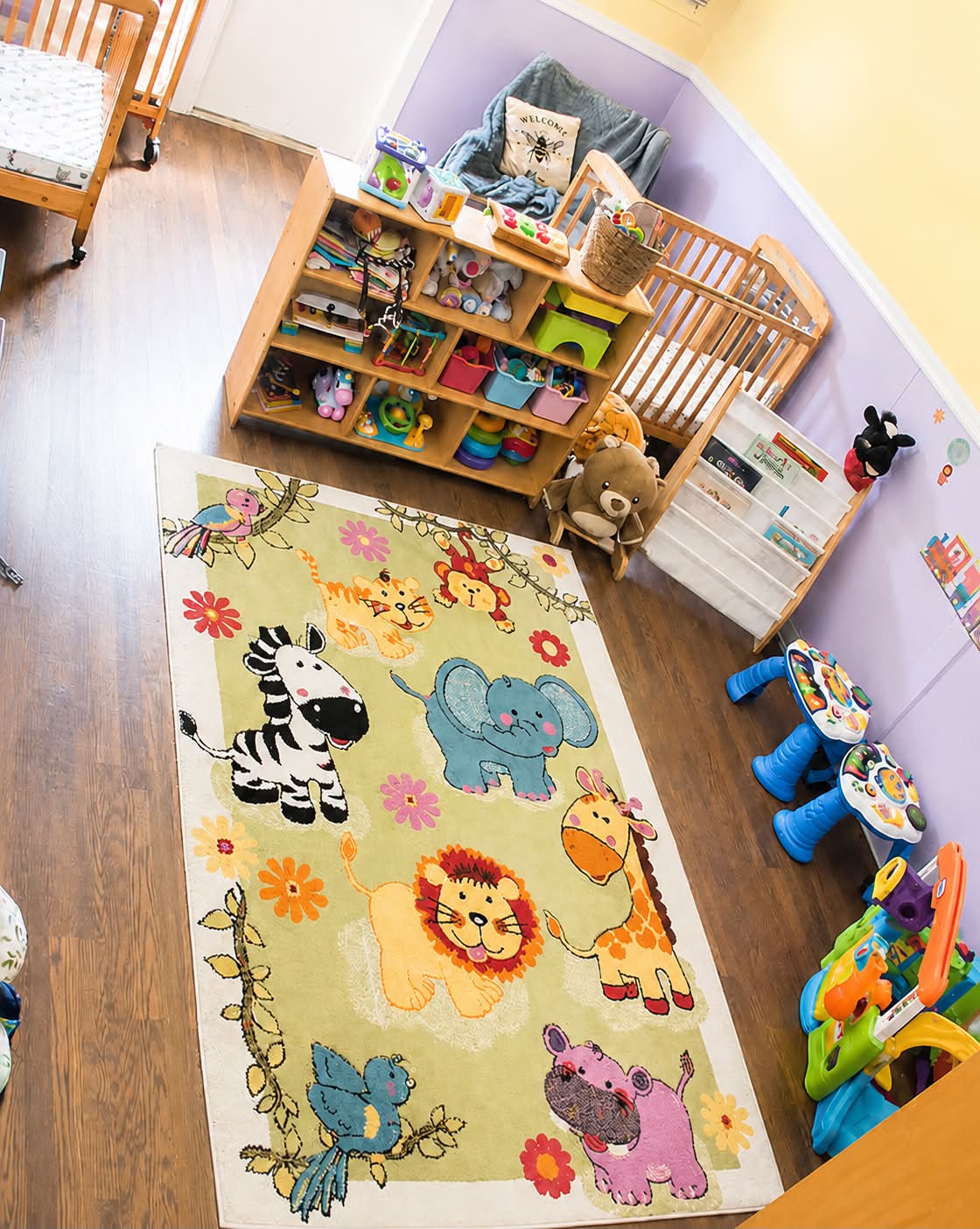 Infant room with wooden cribs, toy shelves and a jungle animal rug